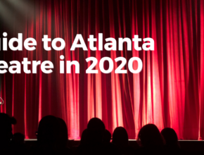 Lights illuminate a closed, red curtain with audience members waiting in the house of a theatre.